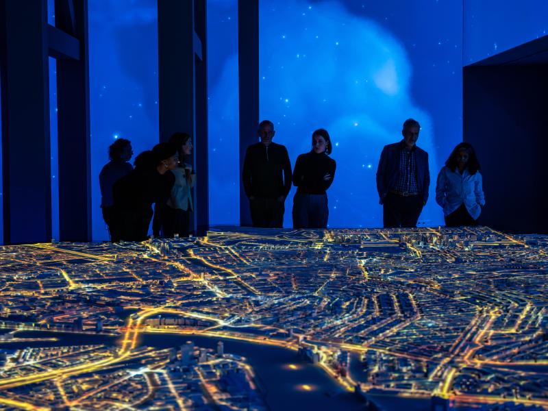 Bezoekers rond het verlichte stadsmodel in de avond