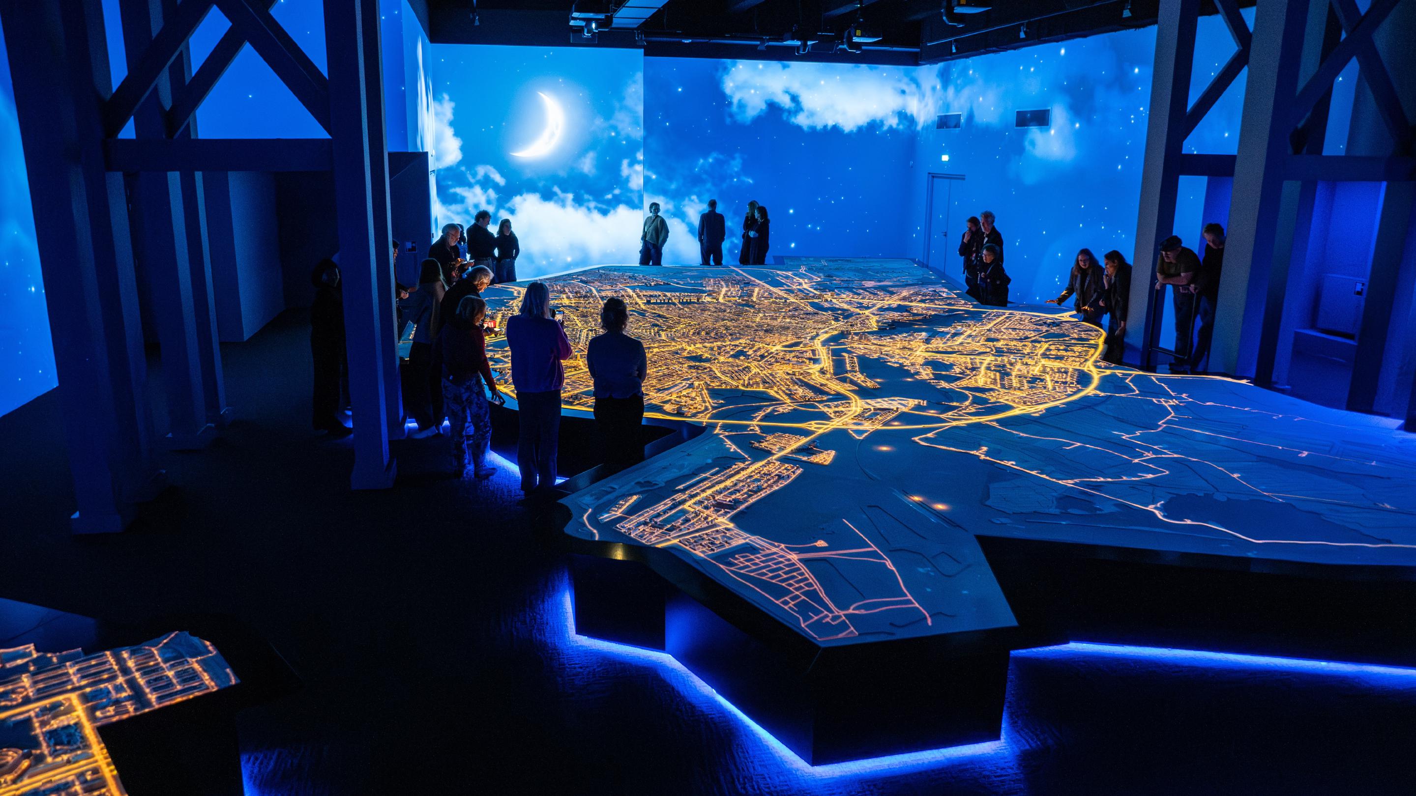 Bezoekers rond het verlichte stadsmodel van Amsterdam in Motion